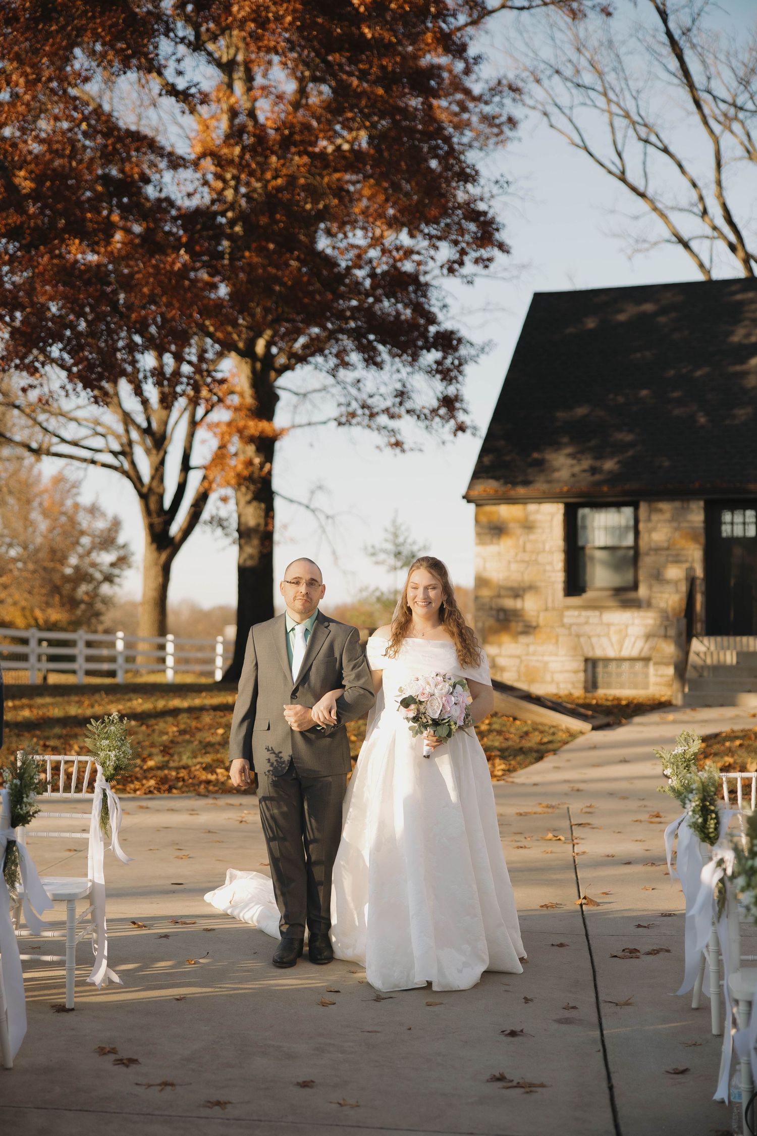 A wedding ceremony setup with white chairs and stone buildings in the background during fall season.