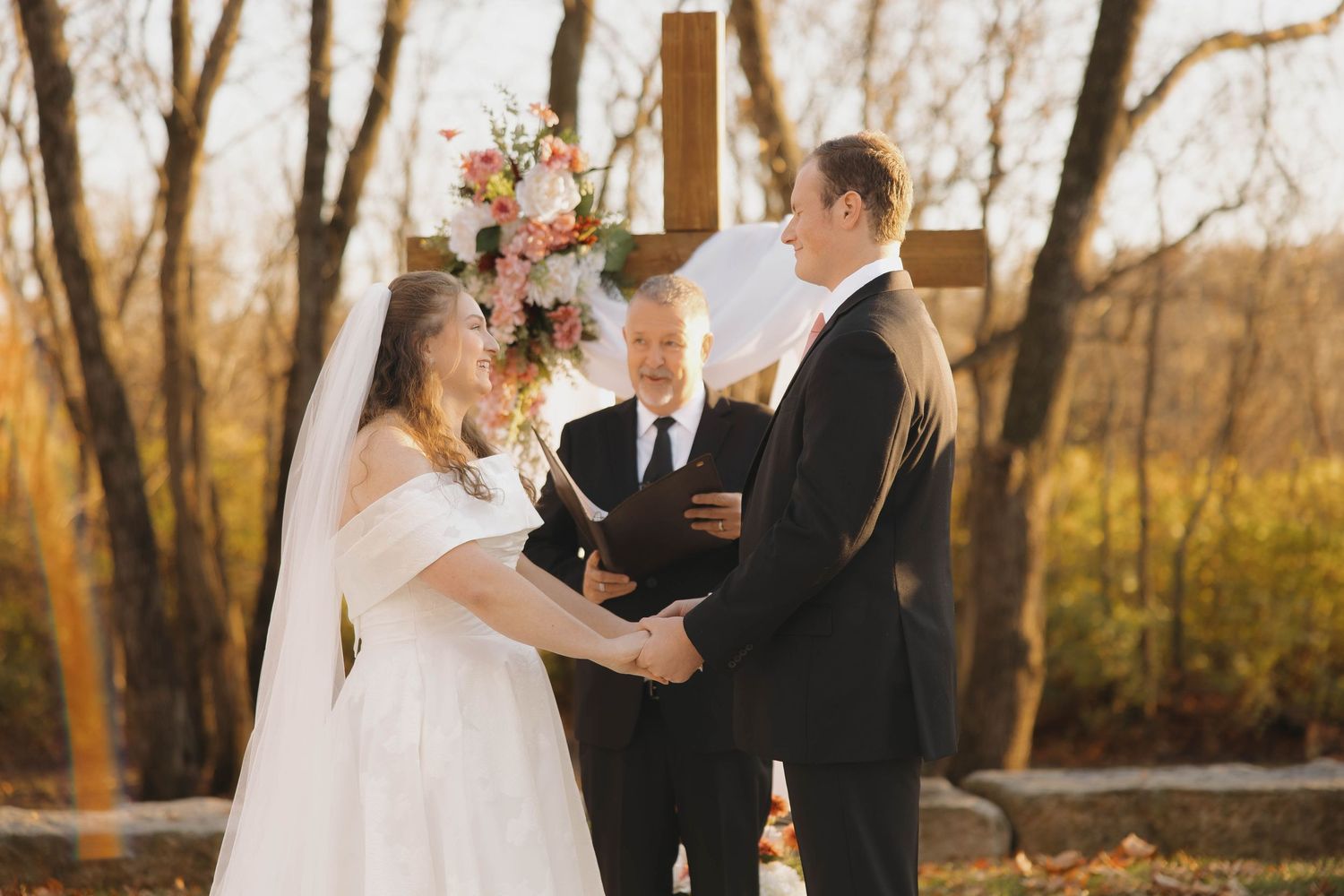 Outdoor wedding ceremony moments with couple exchanging vows among fall trees.