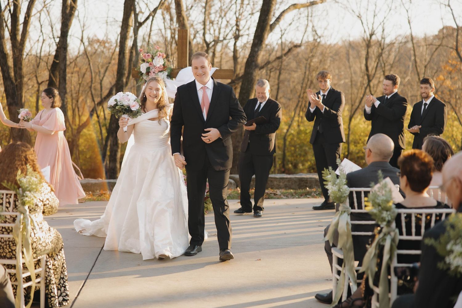 Outdoor wedding ceremony setup with white chairs and autumn trees in the background.