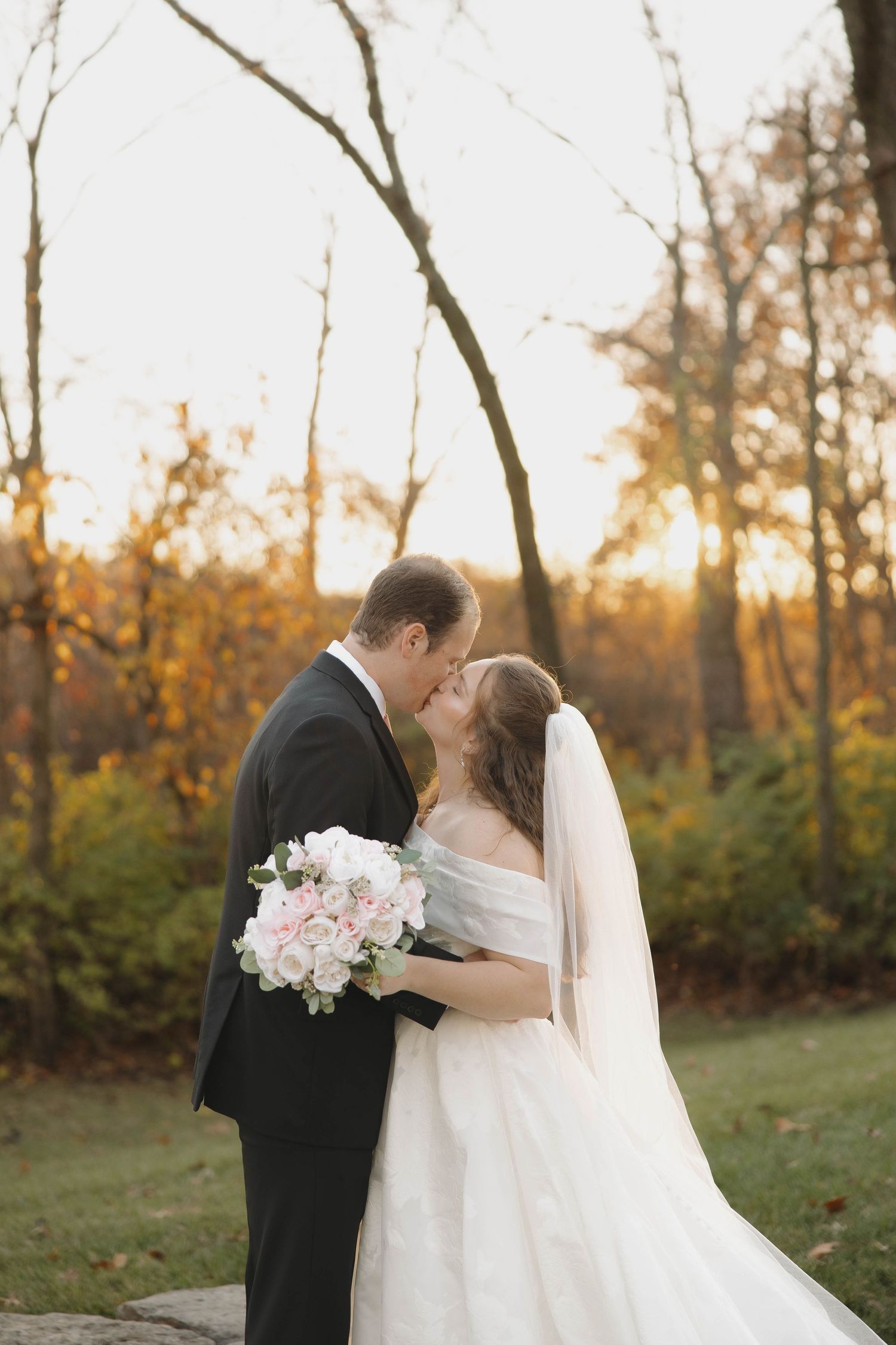 Romantic wedding couple shares intimate moments during sunset photoshoot in autumn setting.