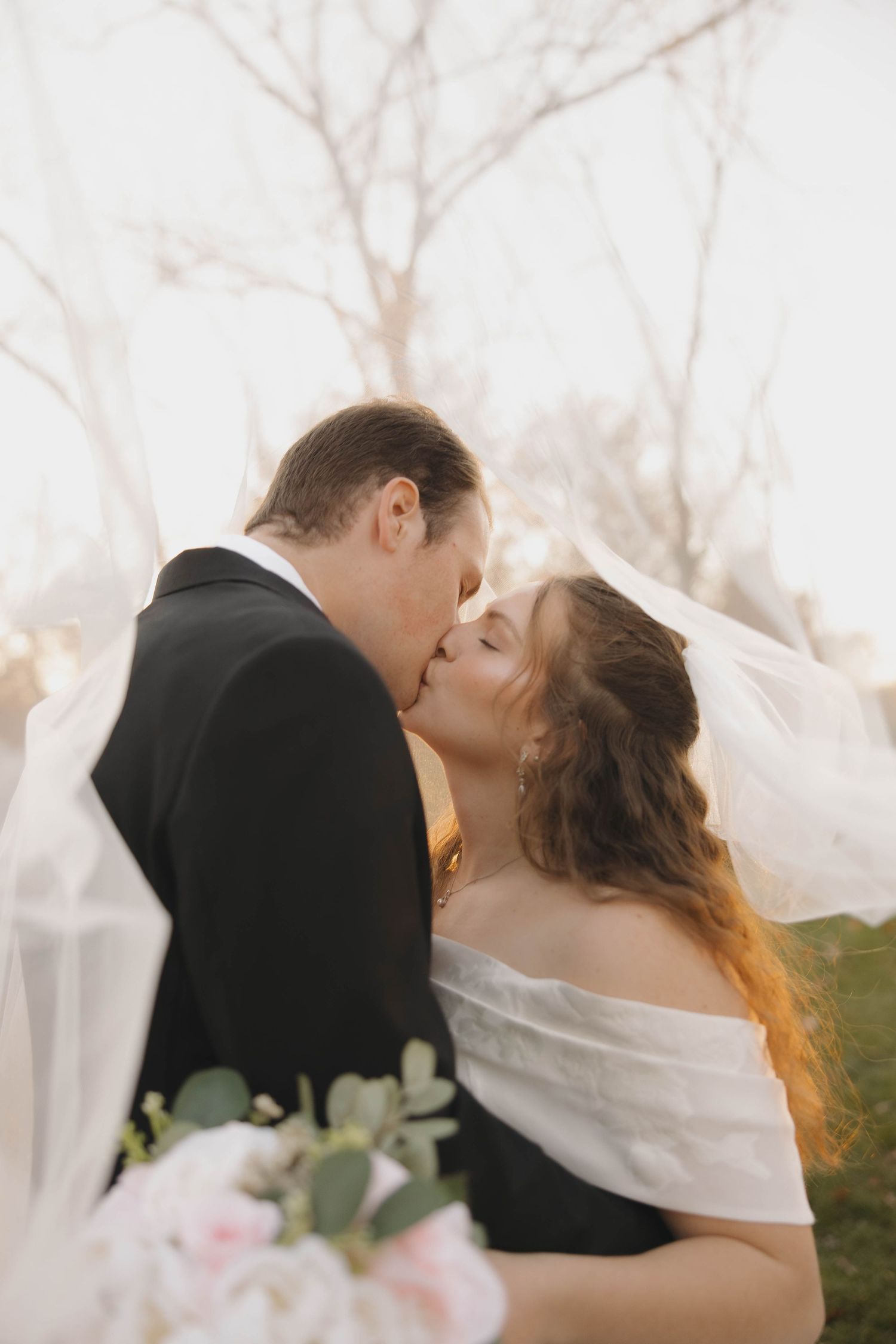 A romantic wedding portrait of a couple sharing a kiss with soft lighting and pink floral bouquet.