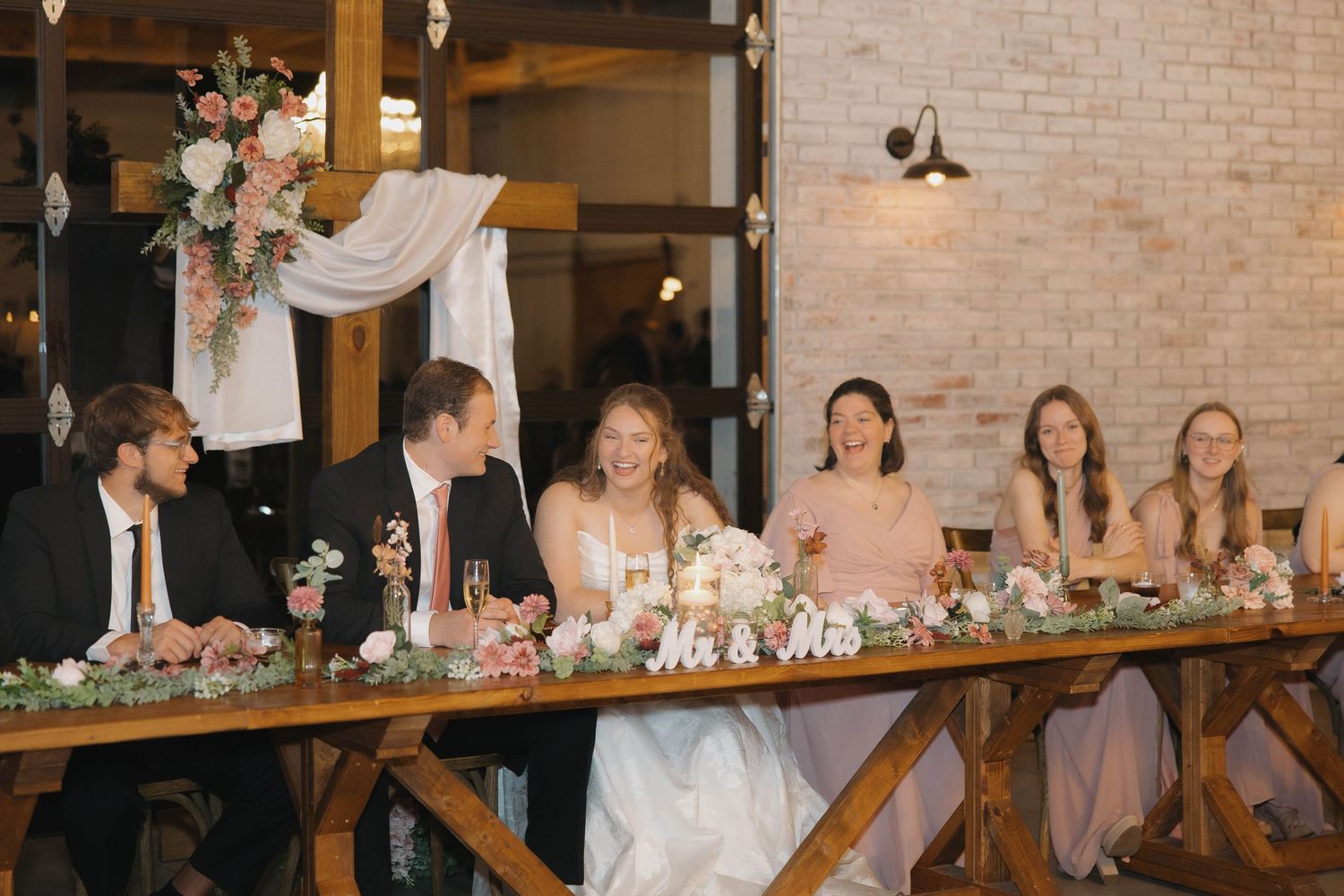 Wedding reception tables decorated with floral arrangements and candles in an elegant rustic brick-walled venue.