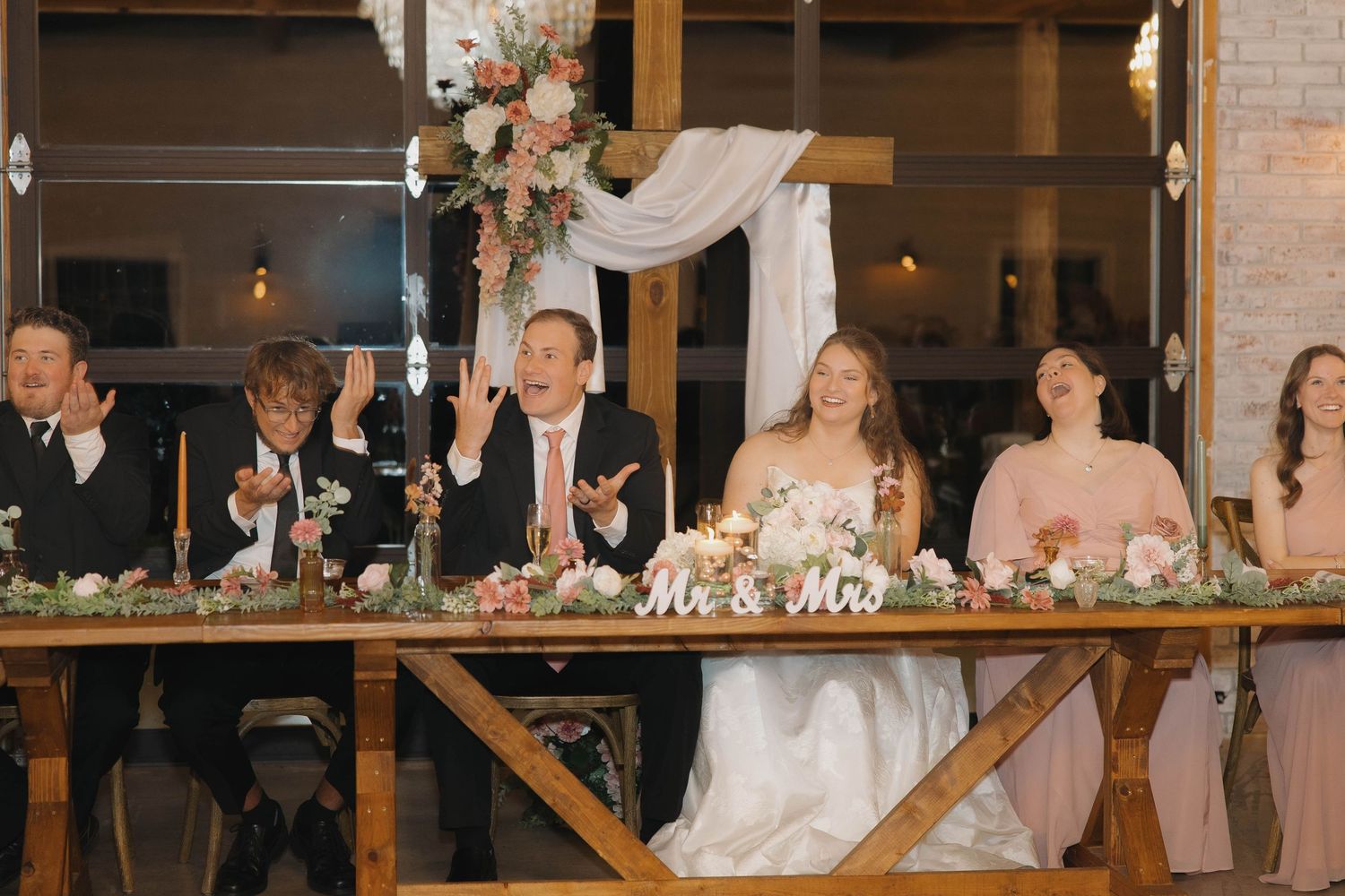 Wedding reception setup in rustic brick venue with elegant table settings and hanging lights.
