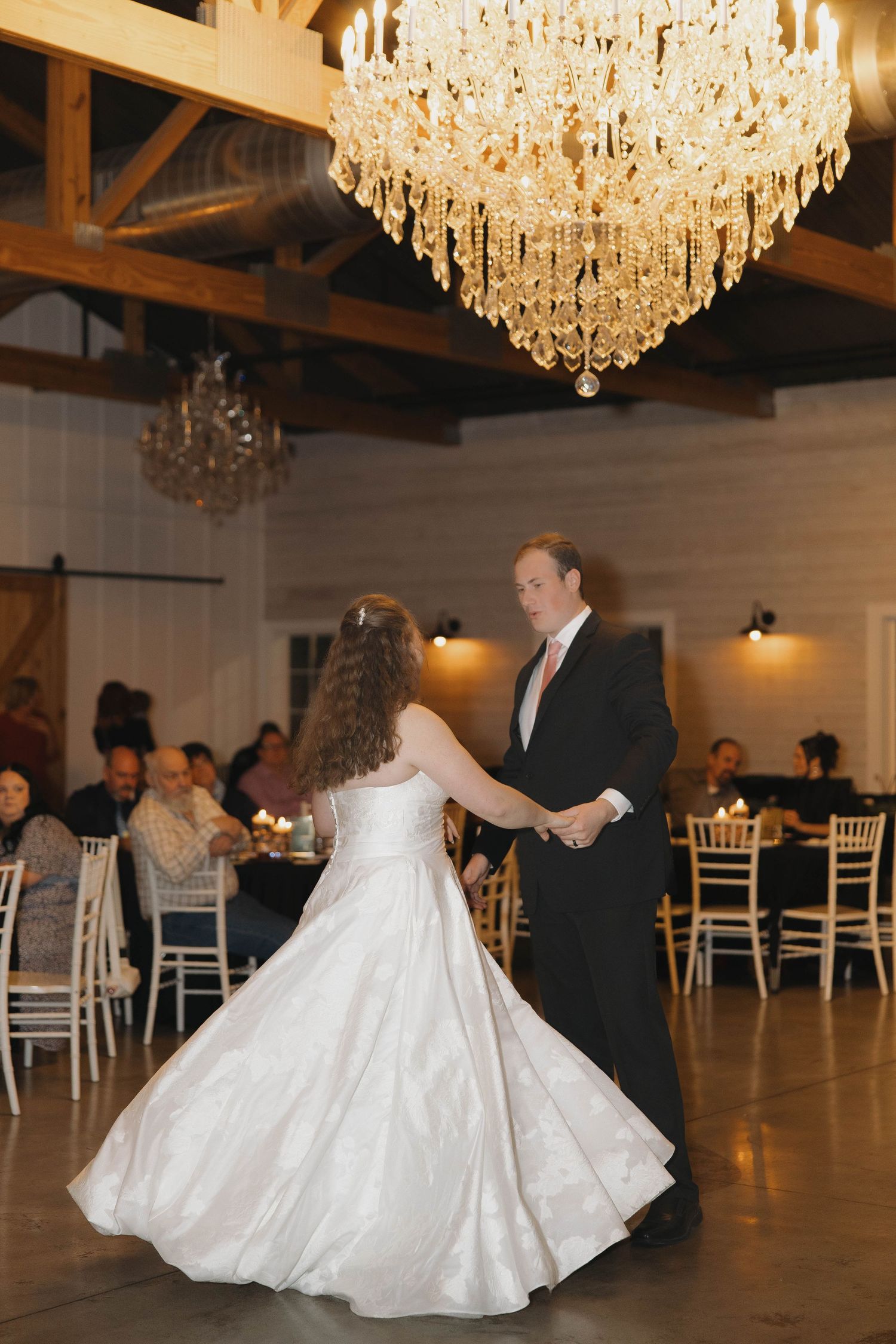 Elegant ballroom reception with crystal chandeliers and a couple dancing on the white dance floor.