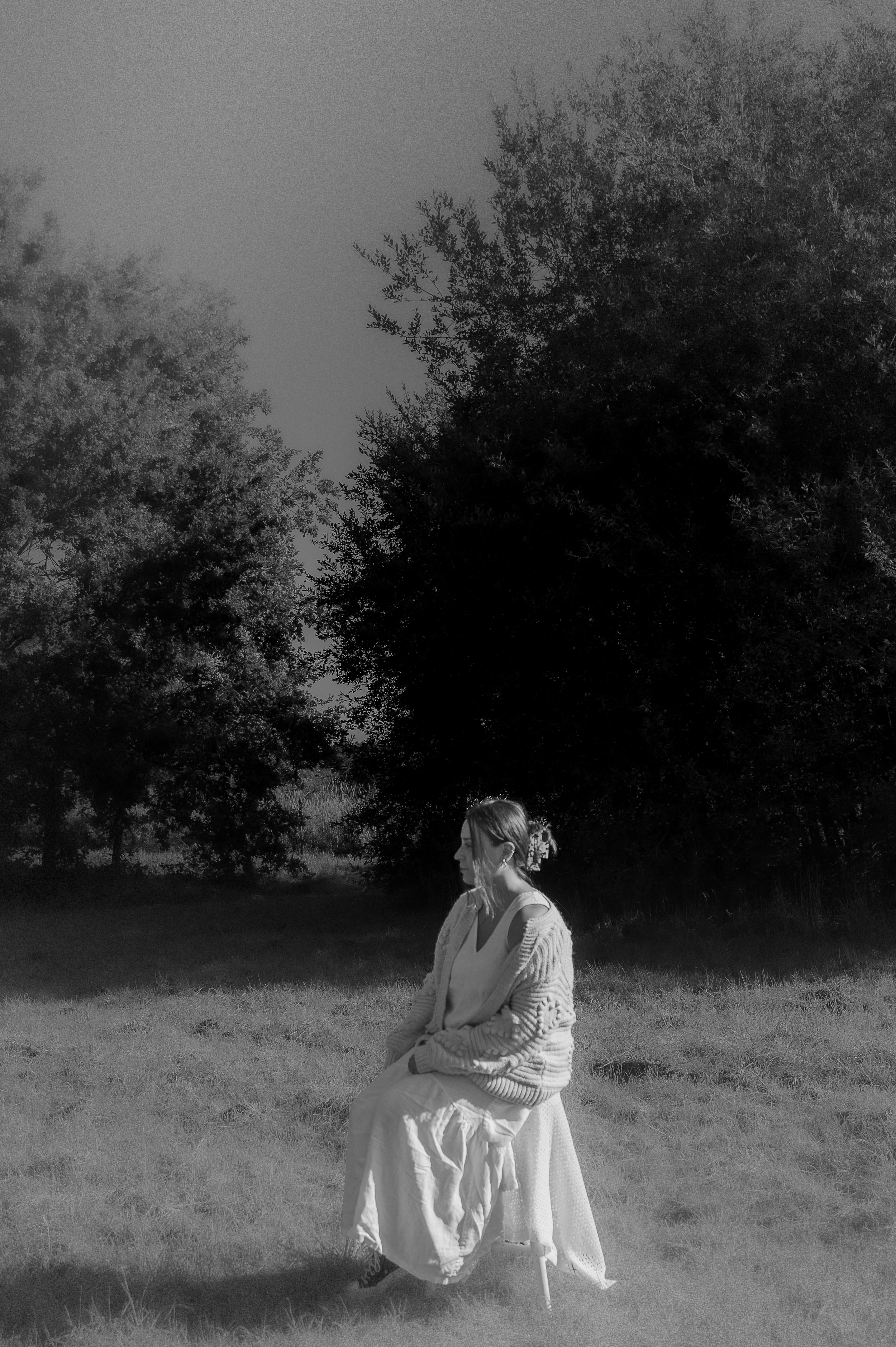 A sequence of black and white photographs showing a person in white clothing sitting in a grassy field near trees.