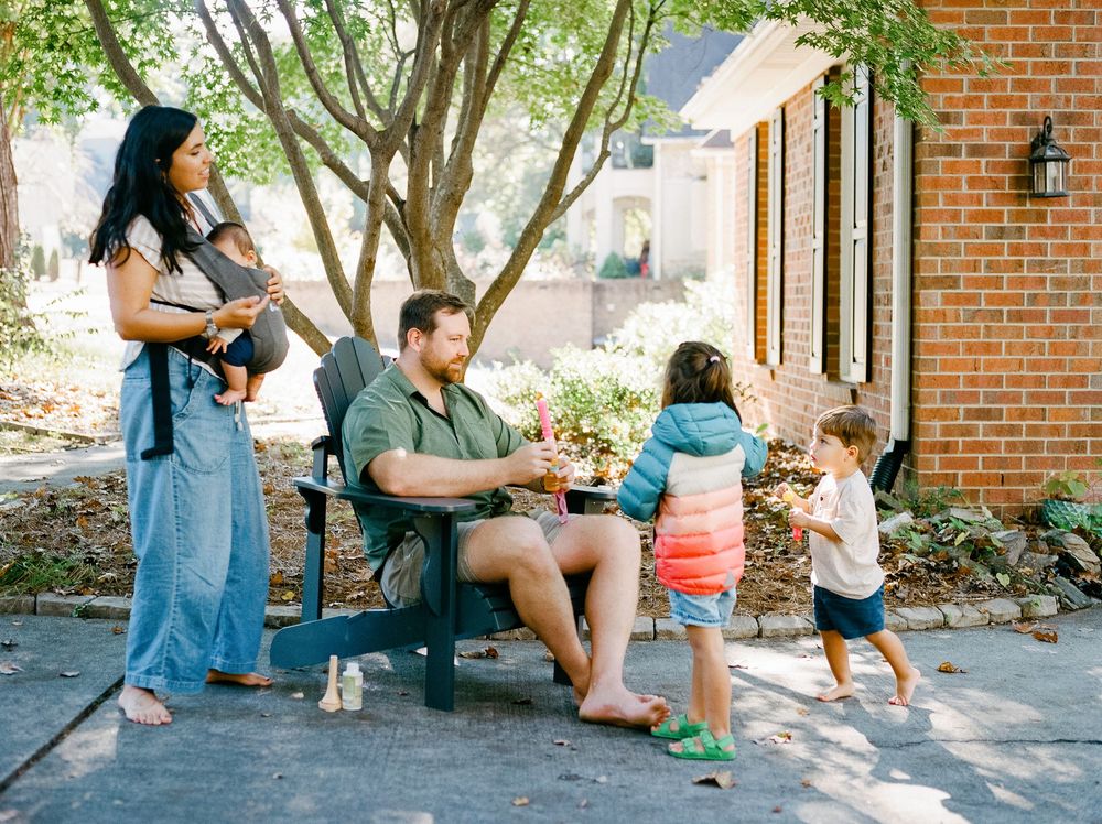 People gather and relax on outdoor benches in a shaded brick courtyard area on a sunny day.