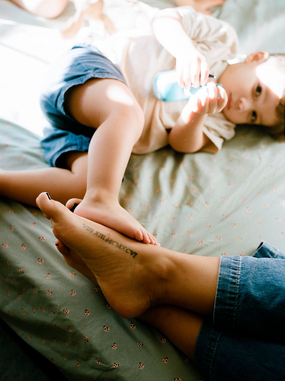 A baby lies on soft bedding wearing white clothing while being gently touched by an adult hand.