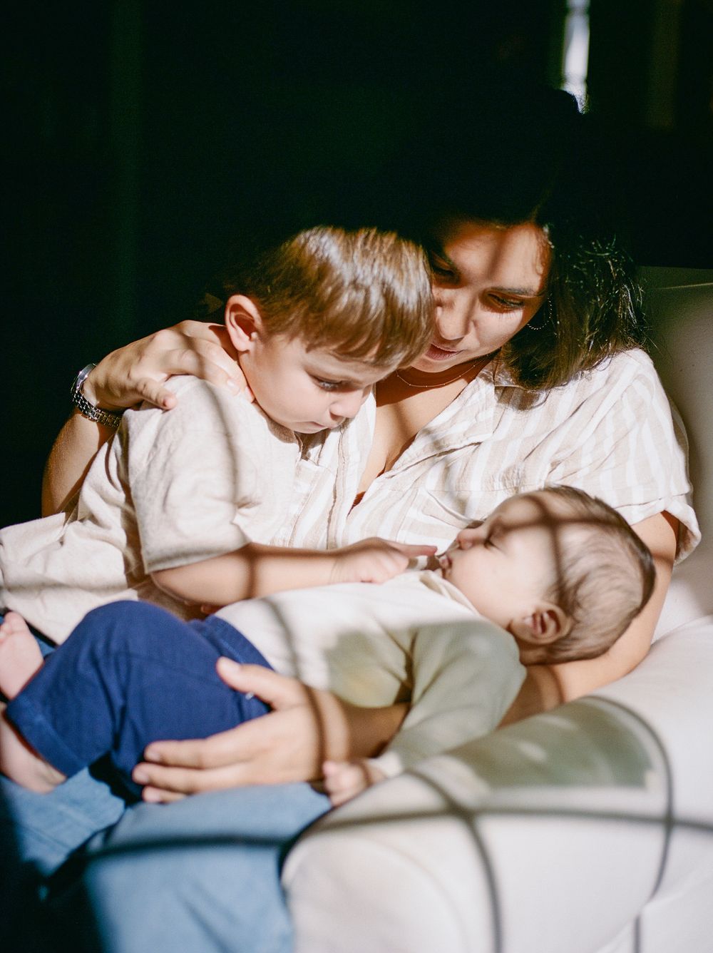 A tender family moment shows gentle interaction on a couch in soft natural lighting.