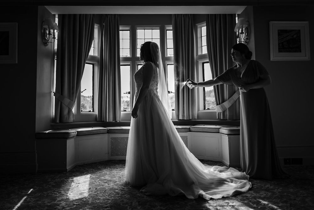 A silhouetted figure in a wedding dress stands in front of a bright window in a dramatic black and white composition.