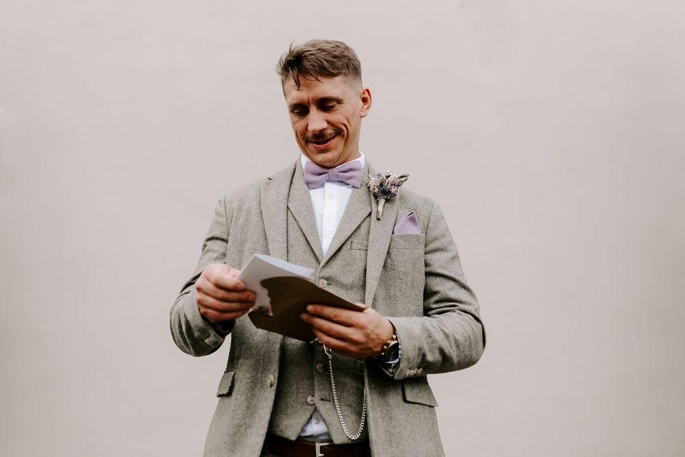 Person in light gray suit and white shirt stands while holding and looking at papers in a professional setting.
