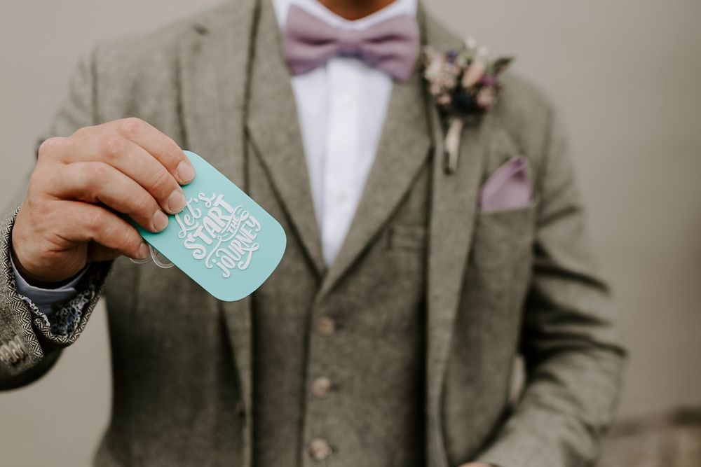 A person in a grey suit and pink bow tie holds a turquoise flask while getting ready for a formal event.