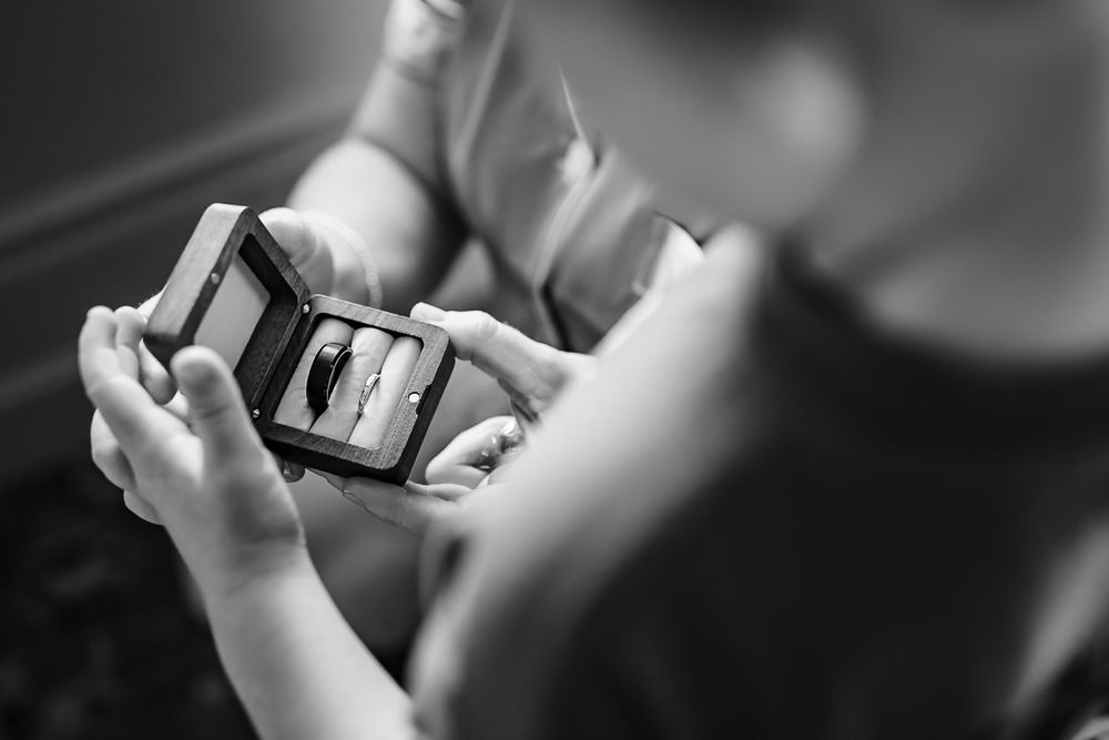 Black and white photo of hands holding a smartphone showing an engagement ring in a jewelry box.