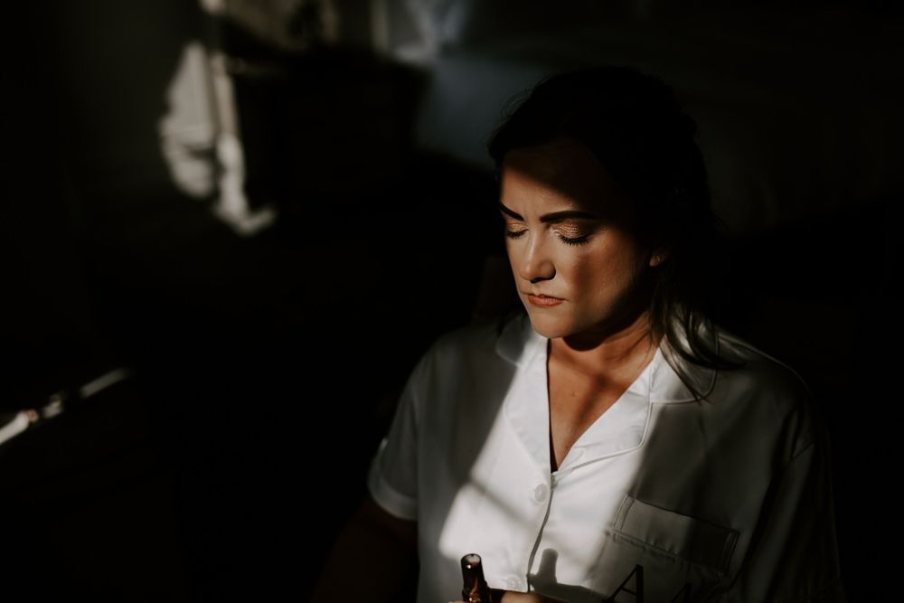 A person in a white shirt and gray jacket stands in dramatic lighting with shadows casting across their face.