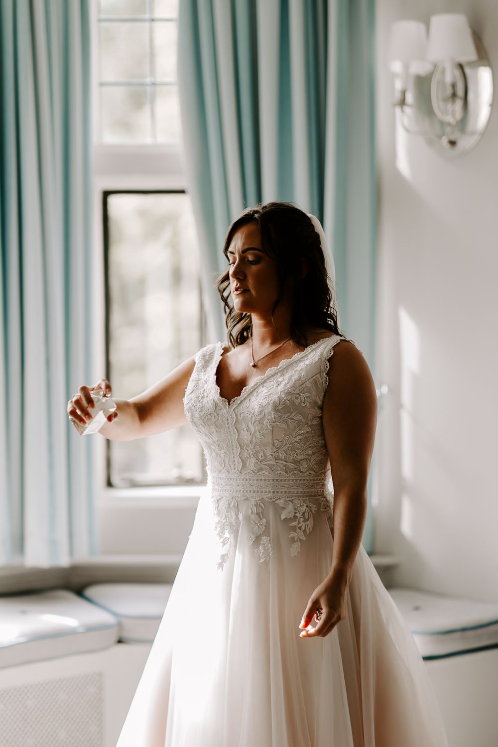 Bride in a flowing white lace wedding gown with empire waist twirls gracefully in a bright room with mint curtains.