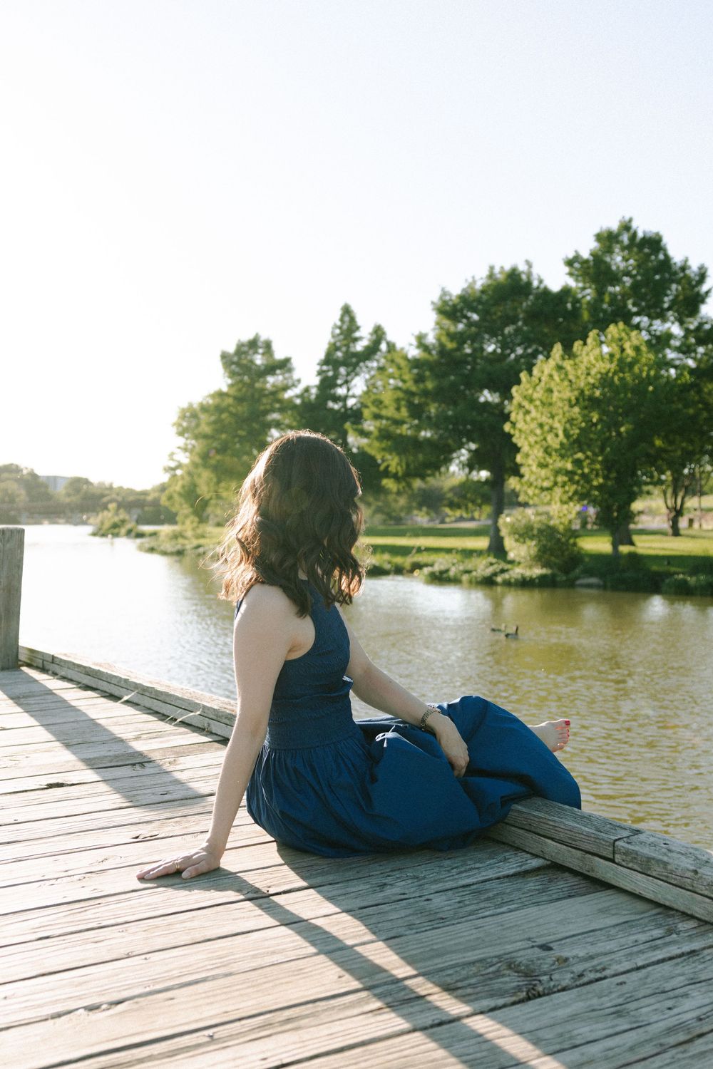 A relaxed summer portrait on a lakeside dock showcasing a navy dress and natural scenery.