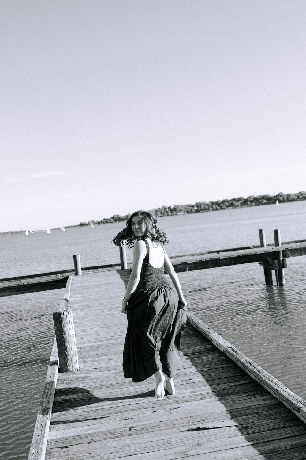 Black and white photo of someone walking on wooden pier by calm waters.