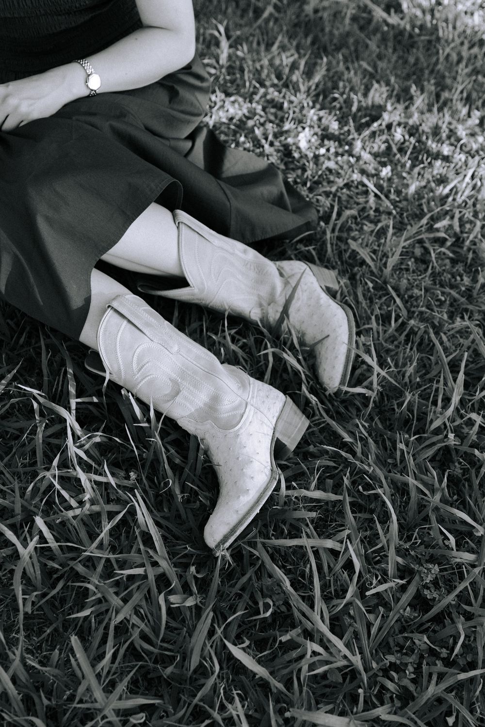 Black and white detail shot of western-style boots and dress hem in grass.