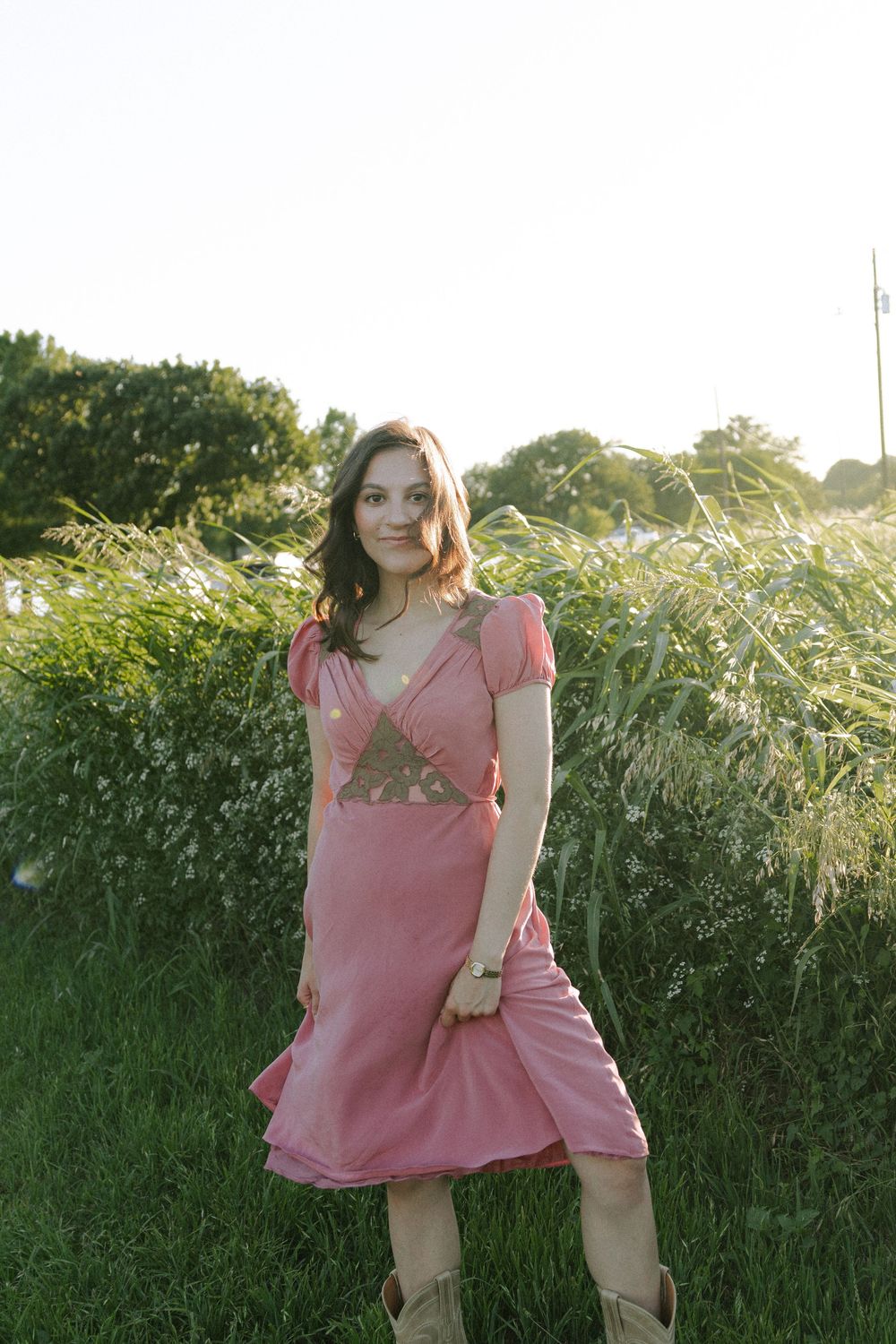 Playful pose in a pink summer dress against natural outdoor backdrop.