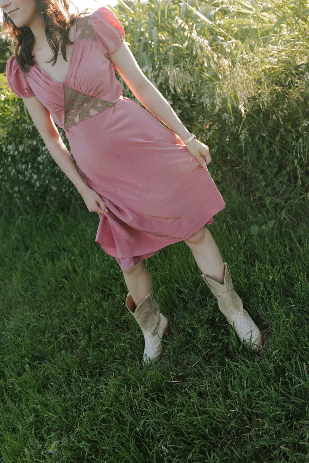 Pink vintage dress paired with cream cowboy boots photographed against tall grass at golden hour.