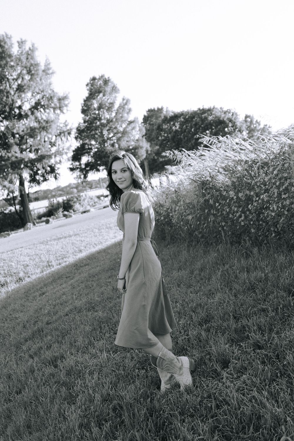 Black and white portrait of woman in dress posing on grassy hillside.