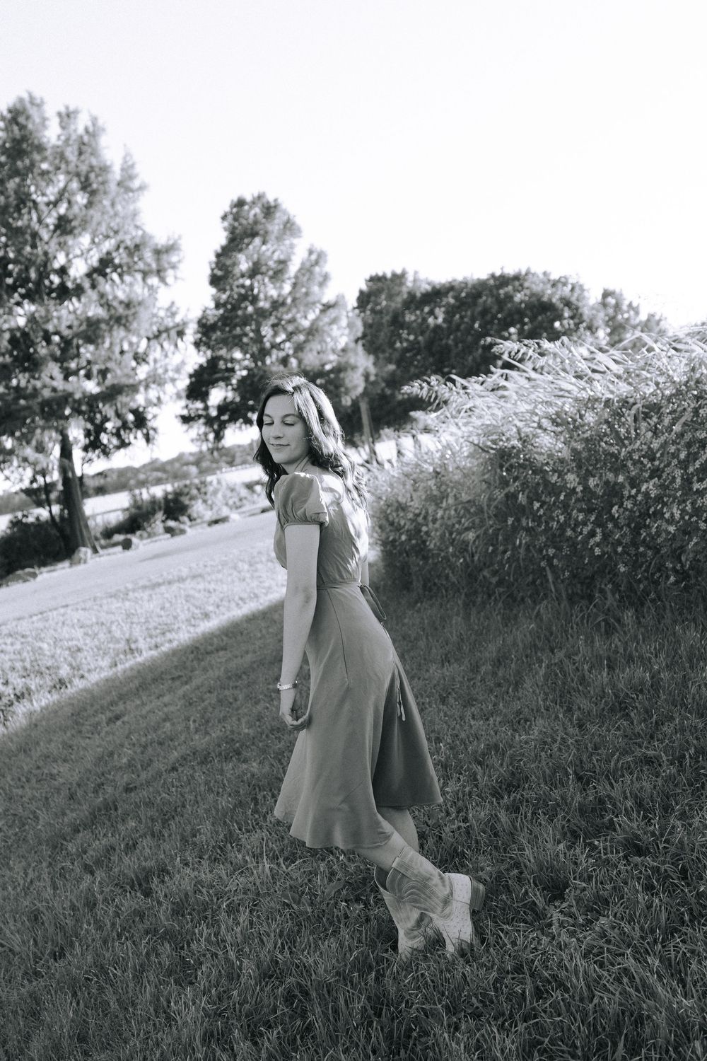 Black and white photo of woman in flowing dress on hillside.