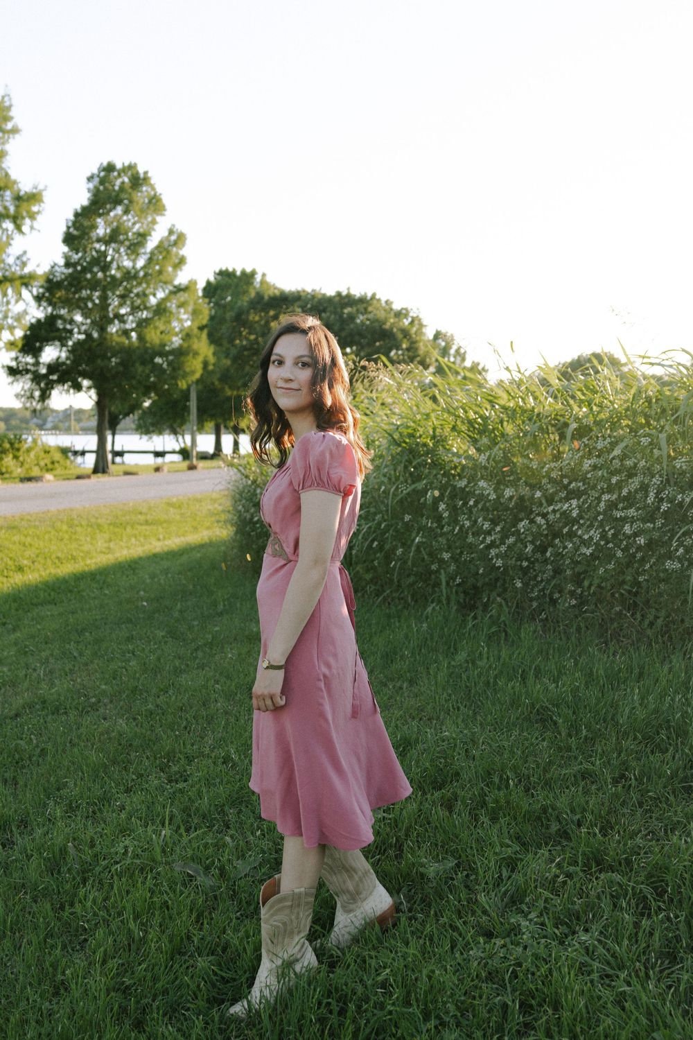 Person in pink dress twirls playfully in a grassy field during golden hour.