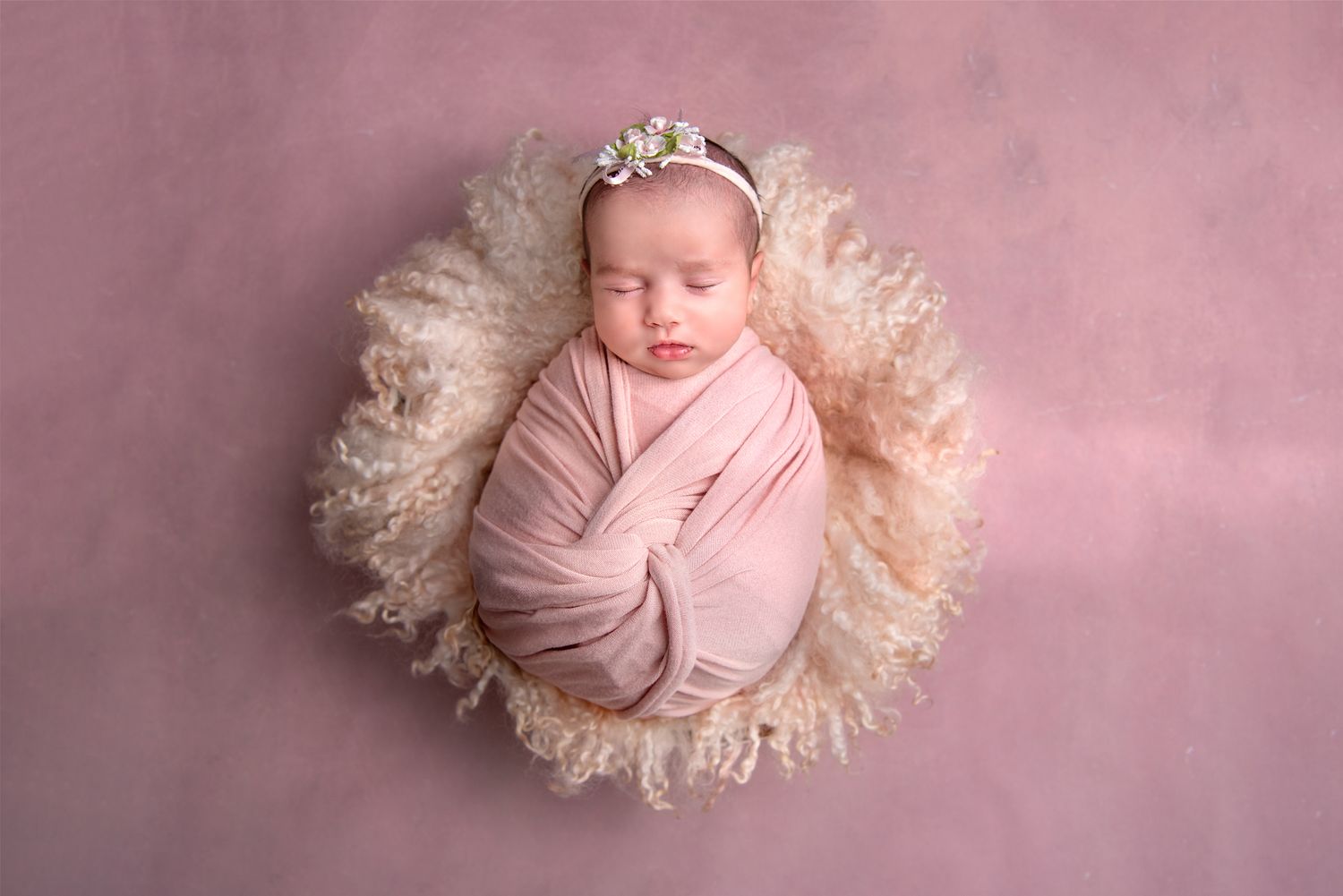 newborn baby girl photography portrait in soft pink tones sleeping on pale pink furry blanket in a bowl against a blush background.
