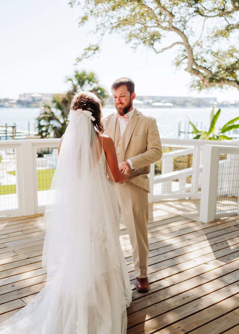 White wedding dress flows gracefully across wooden deck with white railings overlooking waterfront vista.