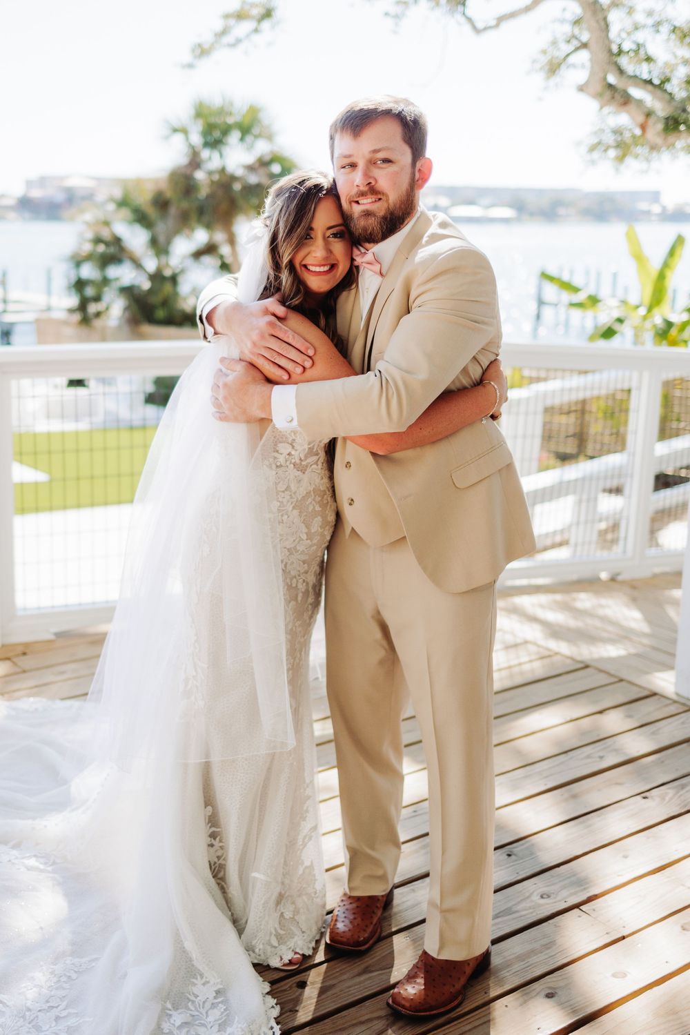 A tender wedding moment as newlyweds embrace on a waterfront deck in beachwear-inspired attire.