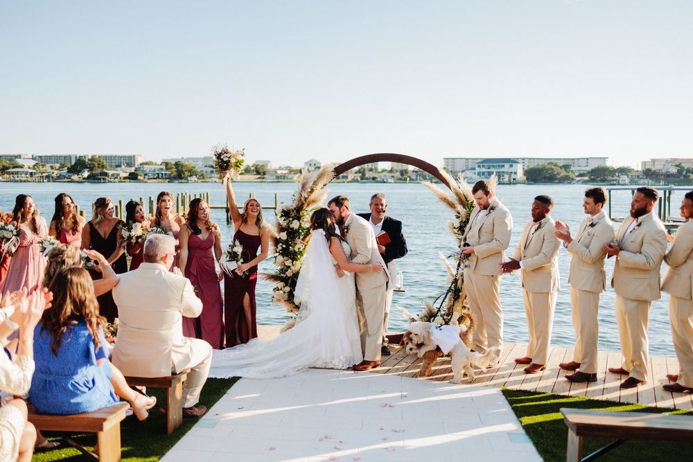 Wedding ceremony setup on waterfront deck with white chairs and floral arrangements.