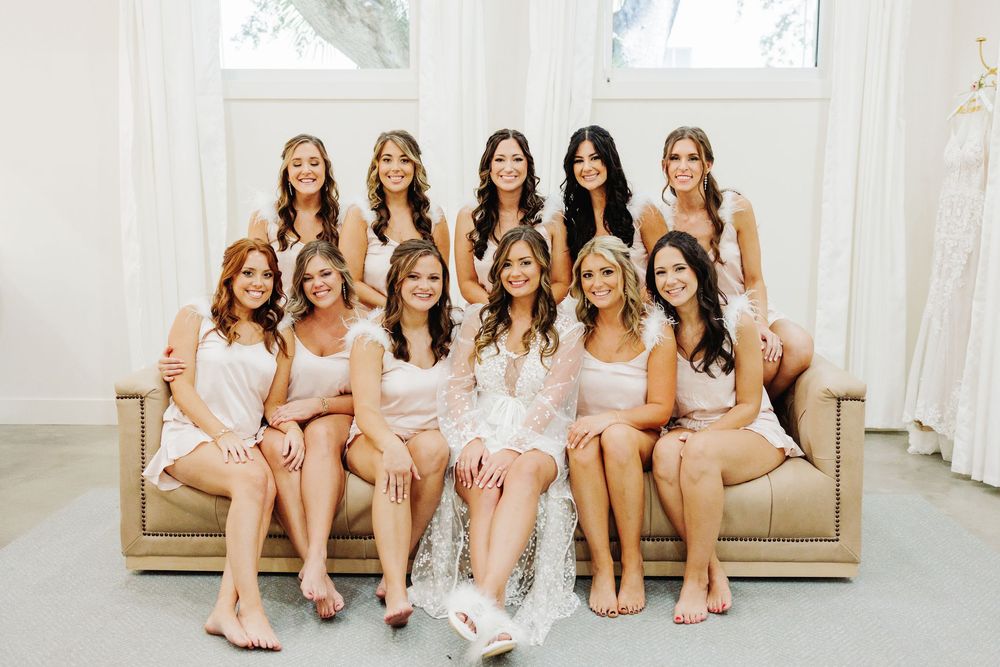 A group in matching satin robes poses together on a beige couch in a bright sunlit room.
