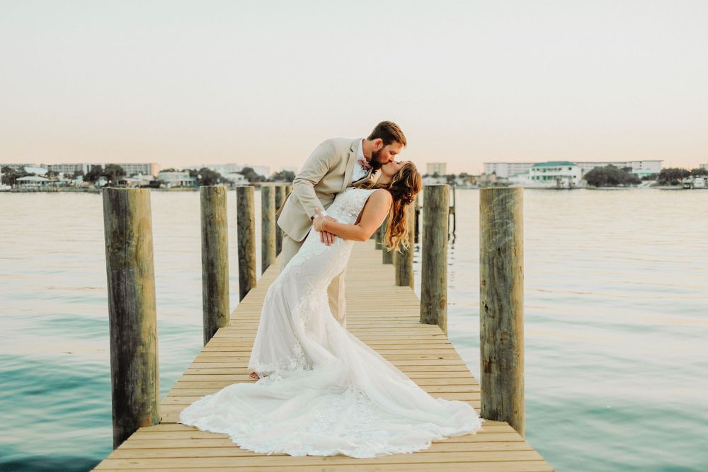 Romantic wedding scene on wooden dock with turquoise waters in background during sunset.