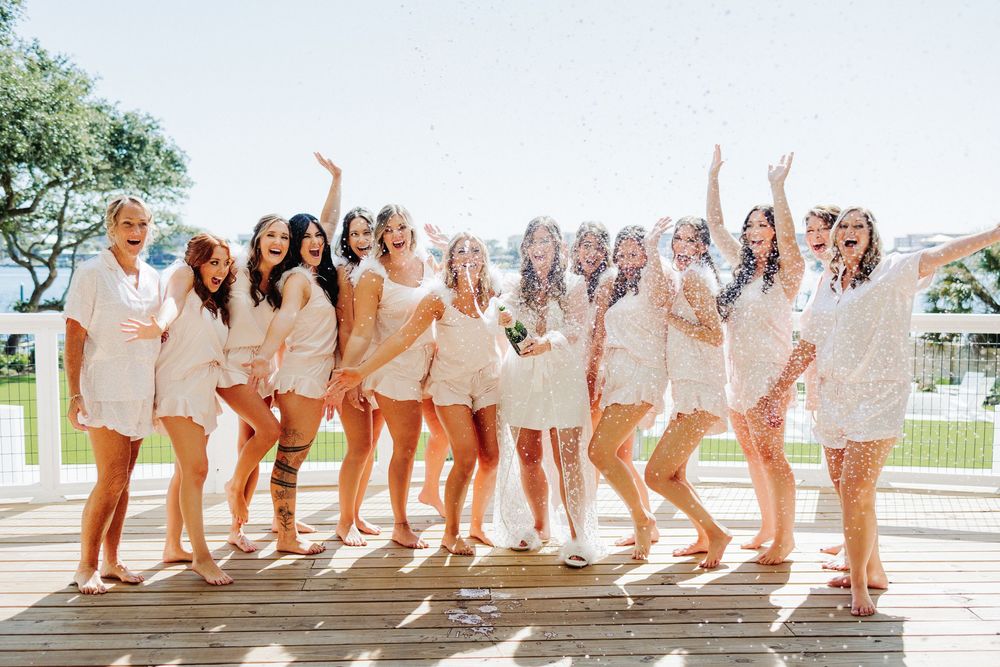 Group in matching cream-colored outfits poses excitedly on wooden deck during a celebratory event.