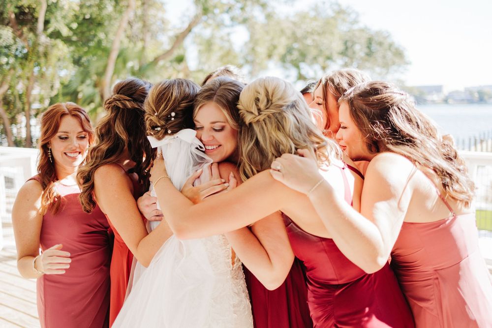 A row of bridesmaids in burgundy dresses share joyful moments together during outdoor wedding celebrations.