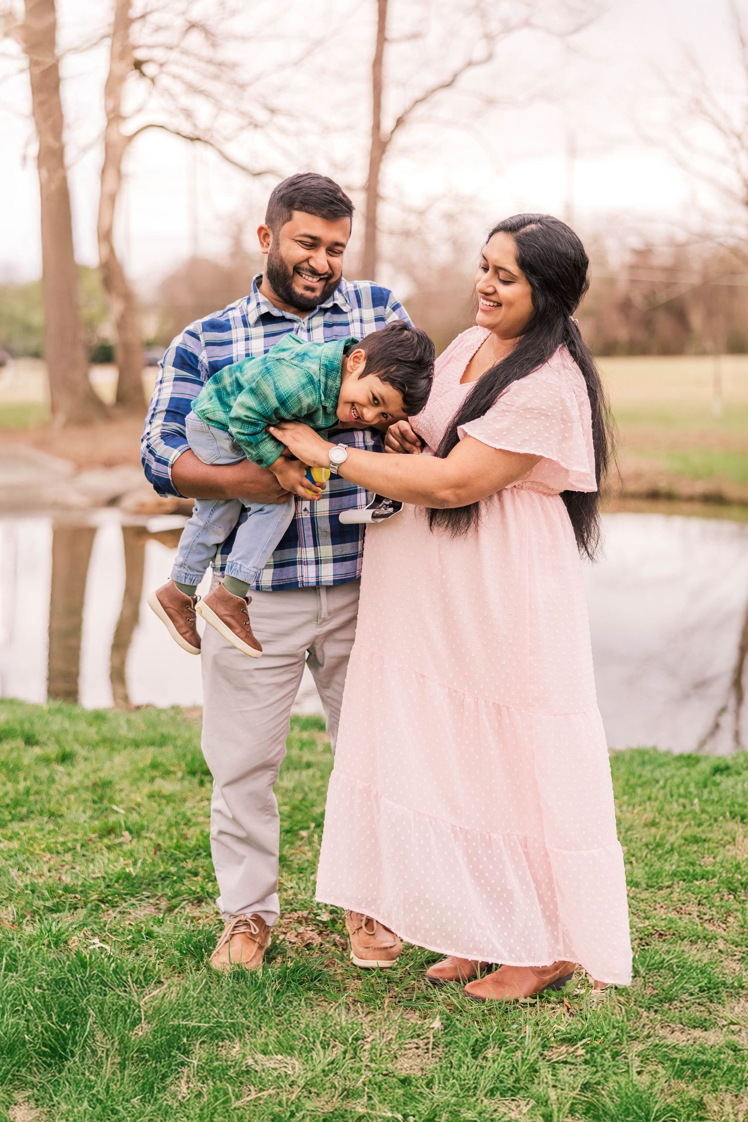 A family shares a tender moment while laughing together outdoors near a pond.