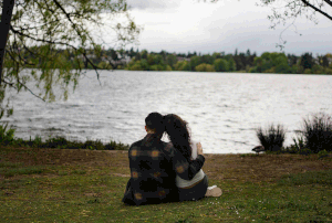 Seven sequential photos show a peaceful lakeside scene with someone lounging on the ground against an overcast sky.