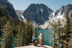 A couple shares a romantic proposal moment on a cliff overlooking Colchuck Lake in the Cascade Mountains of Washington.