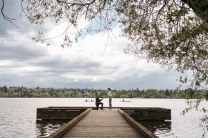 A scenic wooden dock extends into Lake Washington with cherry blossoms framing the cloudy Seattle skyline view.