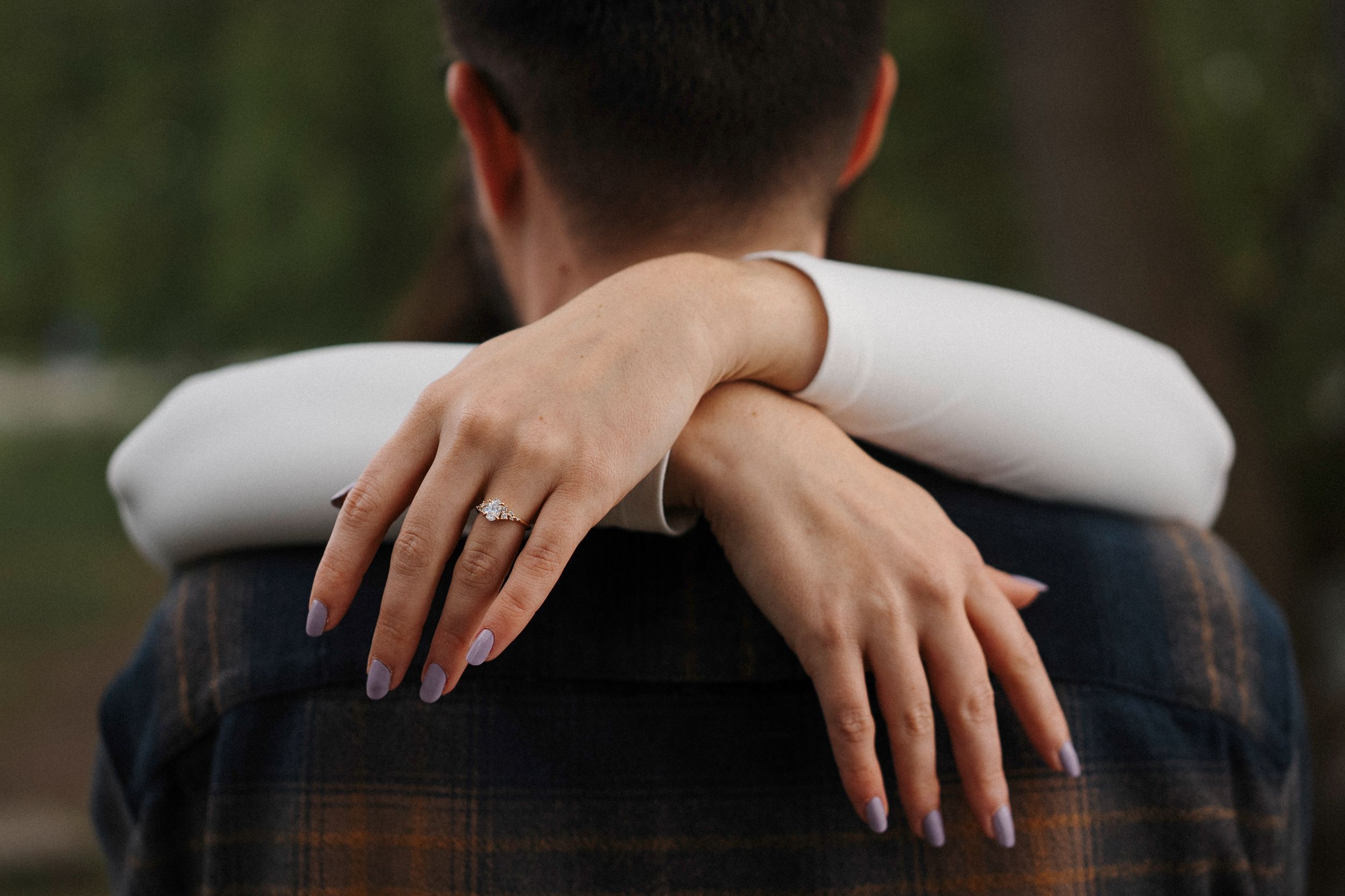 Close up of hands resting on a backrest with a golden wedding ring visible against dark clothing.