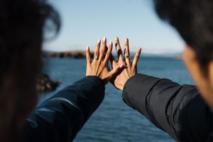 Silhouetted hands are raised against a blue ocean background in a celebratory gesture.