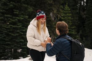 A couple shares a heartfelt moment together in the snow with evergreen trees in the background.