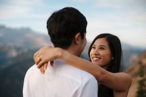 A couple embraces during a romantic photoshoot in a scenic mountain landscape at sunset.