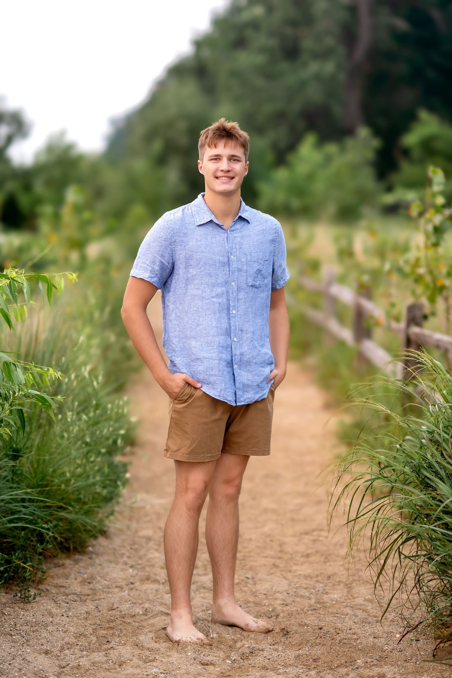 A casually dressed person stands on a dirt path surrounded by summer wildflowers and greenery.