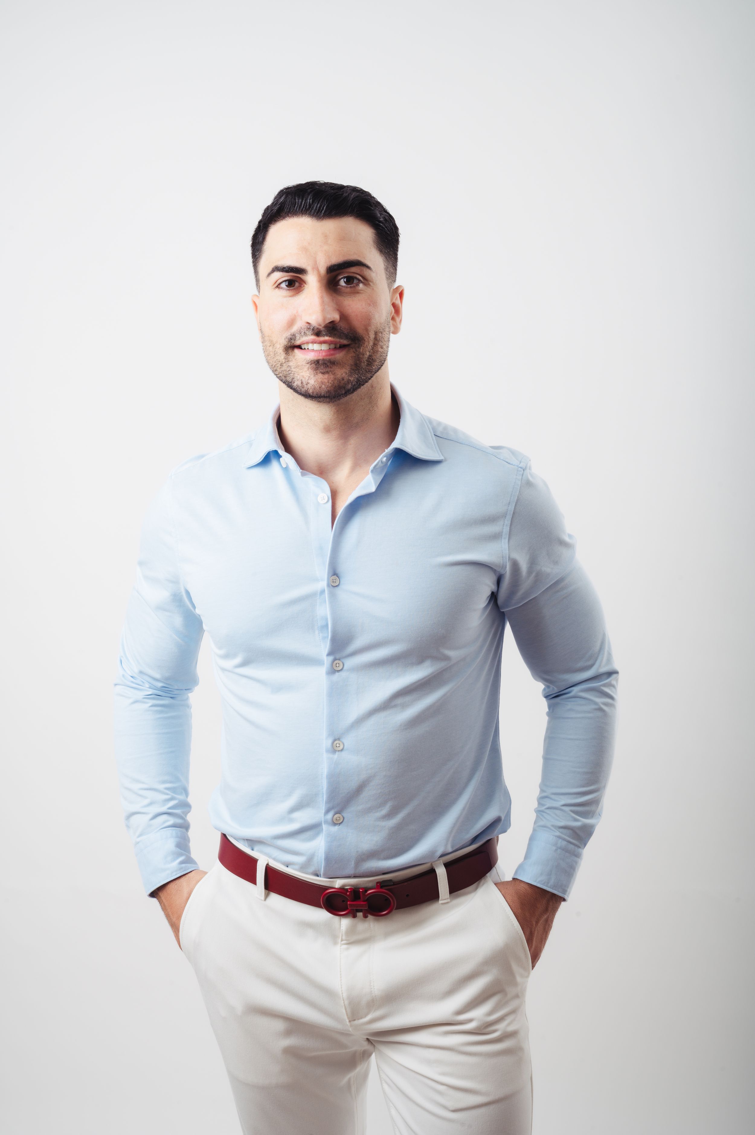 Professional portrait of someone wearing a light blue button-down shirt and white pants against a white background.