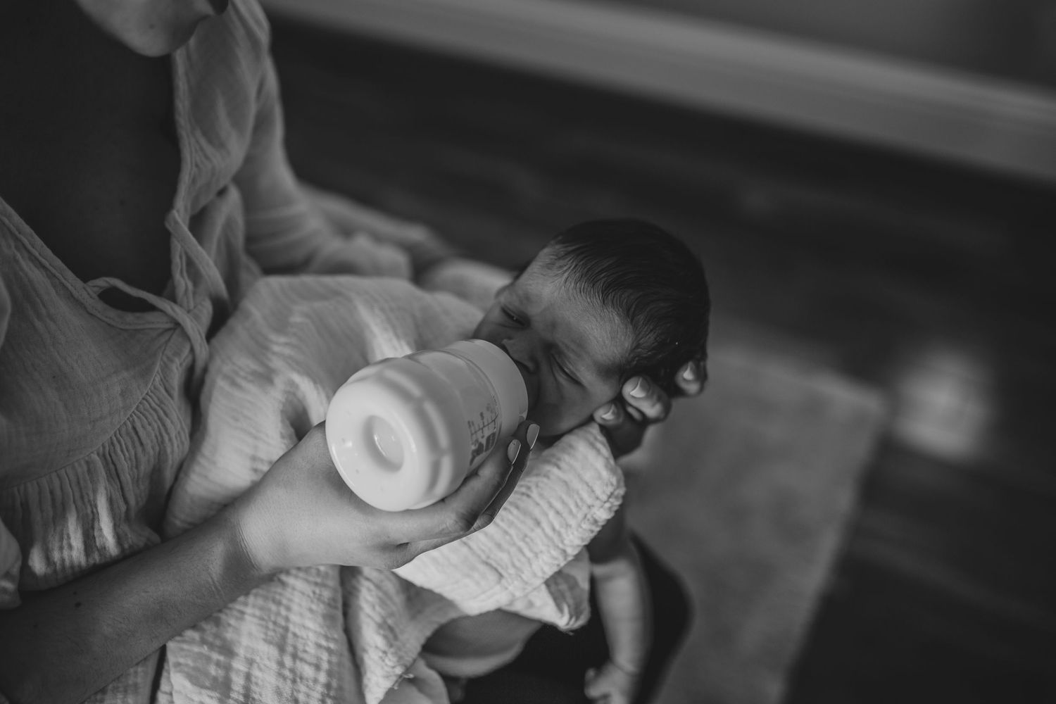 A black and white photograph of an infant being bottle fed while cradled in someone's arms.