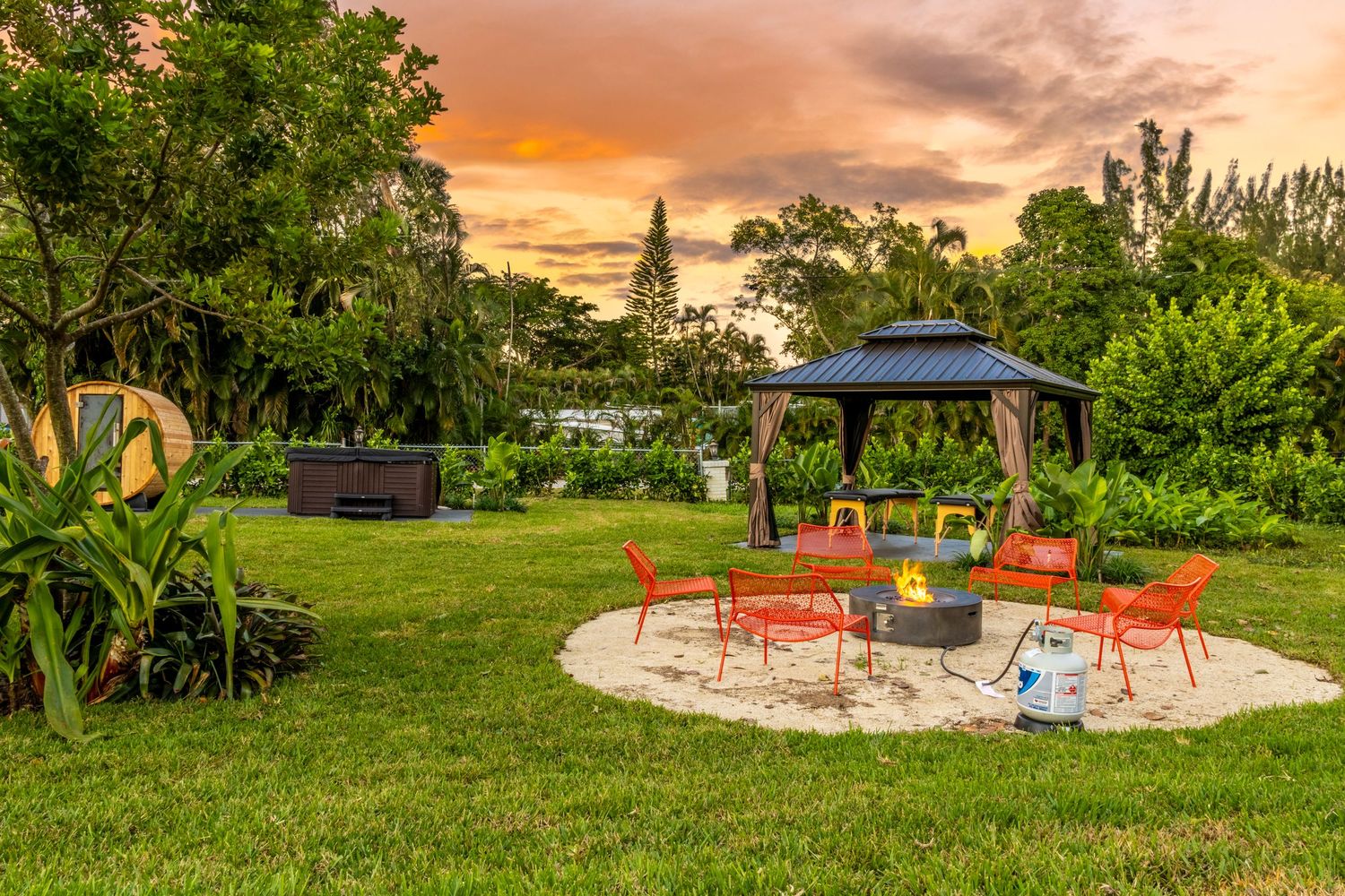 Garden seating area with bright orange chairs and umbrella against dramatic sunset sky.