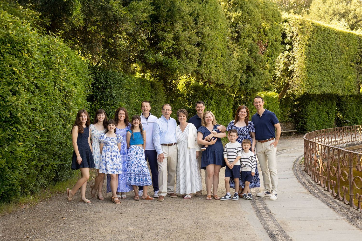 A large multi-generational family group walking together along a scenic outdoor pathway with green foliage.