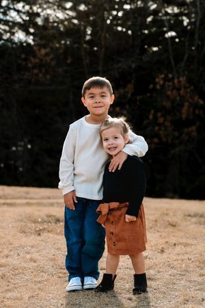 Two young children play together in an outdoor setting with trees in background during a Kearney, NE, family photography session.