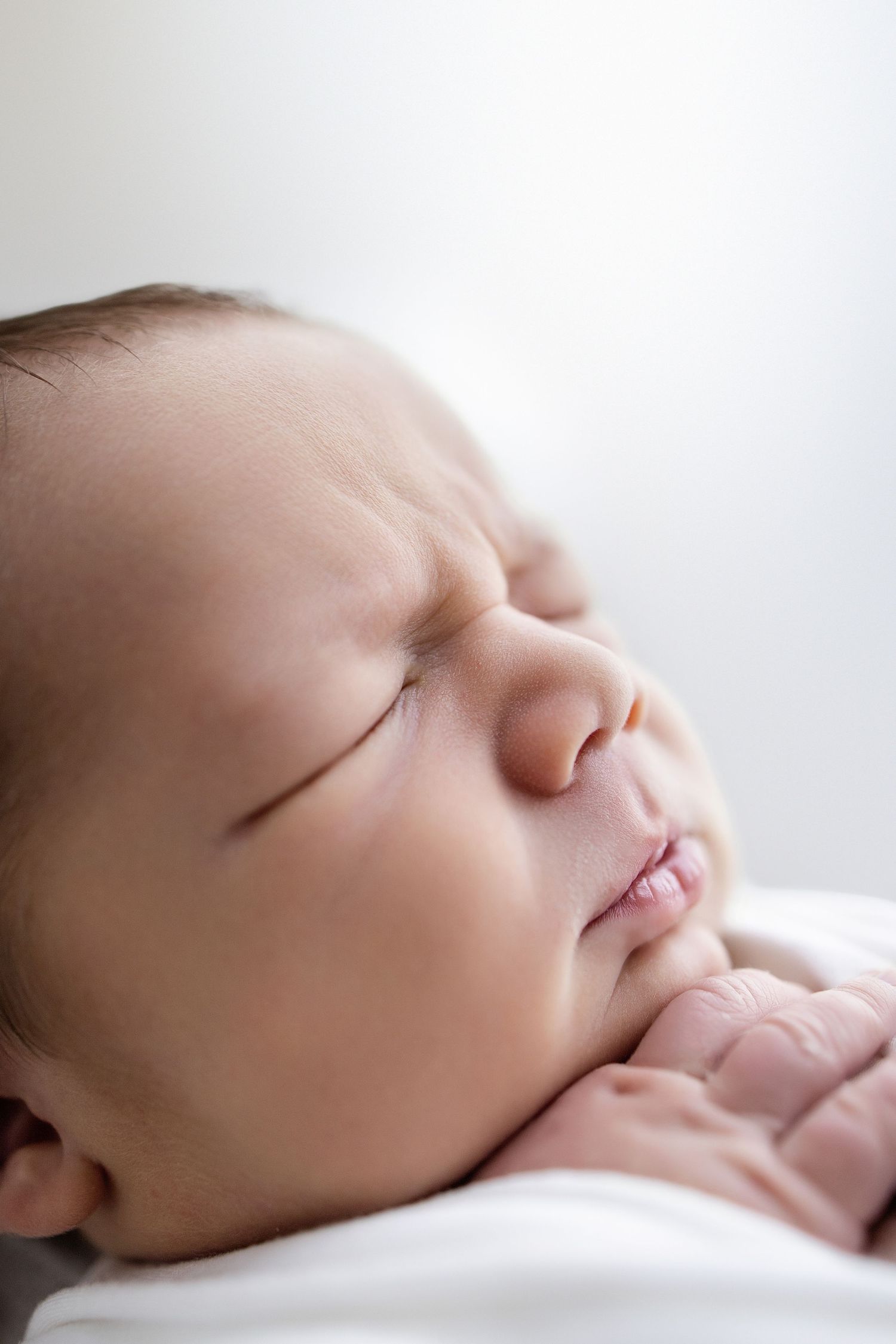 A sleeping newborn wrapped in a soft sage green blanket lies on a woven basket with eucalyptus decor.