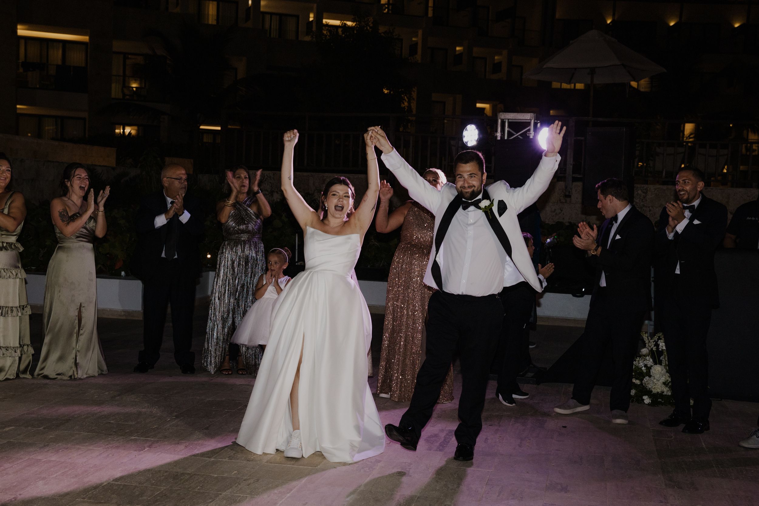 Newlyweds celebrate with joyful dance moves while guests cheer during wedding reception.